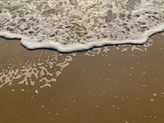 The waves on the sandy beach and white foam with the sunshine in summer morning.