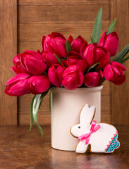 Pink tulips and easter bunny cookie on wooden background.