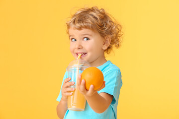 Cute little boy drinking orange juice on color background