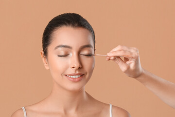 Beautiful young woman undergoing procedure of fake eyelashes applying  against color background