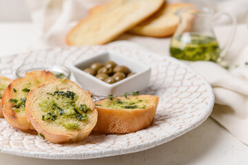 Plate with fresh bread, garlic and olives on light background