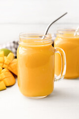 Mason jars of tasty mango smoothie on light background