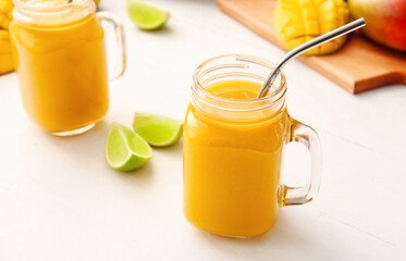 Mason jars of tasty mango smoothie on light background