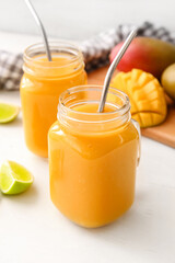 Mason jars of tasty mango smoothie on light background