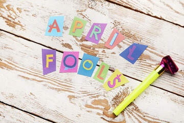 Party horn and text APRIL FOOLS on white wooden background