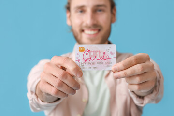 Handsome young man with gift card on color background, closeup