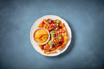 Mexican nachos with chili con carne, guacamole and cheese sauce, top shot on a blue background