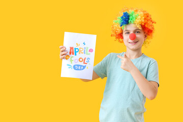 Little boy in funny disguise and with poster on color background. April Fools Day celebration