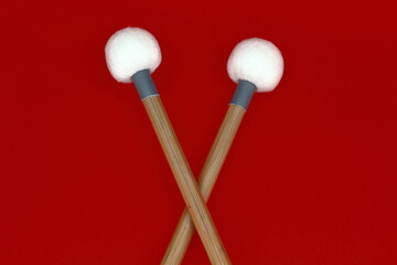 Detail of crossed timpani mallets on a red background.