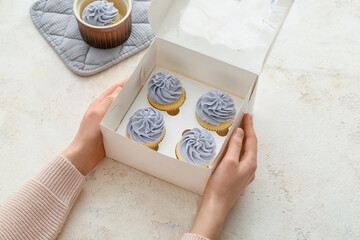 Female hands with tasty cupcakes in box on light background