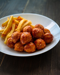 Spicy coated meatballs with spicy sauce served with fried potatoe fries. Korean style snacking.