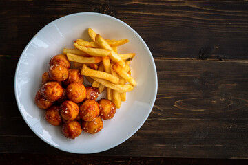 Spicy coated meatballs with spicy sauce served with fried potatoe fries. Korean style snacking.