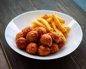 Spicy coated meatballs with spicy sauce served with fried potatoe fries. Korean style snacking.