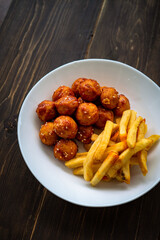 Spicy coated meatballs with spicy sauce served with fried potatoe fries. Korean style snacking.