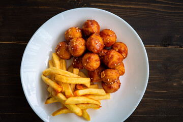 Spicy coated meatballs with spicy sauce served with fried potatoe fries. Korean style snacking.