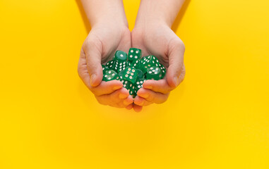 A lot of green dice lie on two hands on a yellow background with space for text: board games, selective focus on the hand, a photo in motion