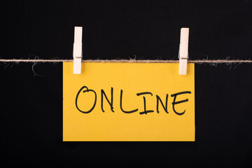 Online word written on a Yellow color sticky note hanging with a wire on black background.
