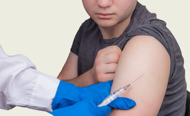 A doctor gives an injection of a coronavirus vaccine to a young guy at the clinic. COVID-19 control concept