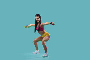 Portrait of a slim woman fitness trainer exercising dumbbell squats with outstretched arms isolated on blue background with copy space