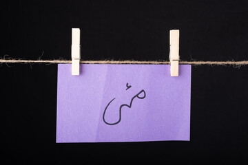 Translation May in urdu word written on a Purple color sticky note hanging with a wire on black background.