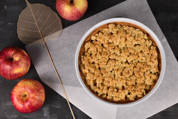 Top view of whole traditional European apple pie with topping crumbles in white springform pan on dark background