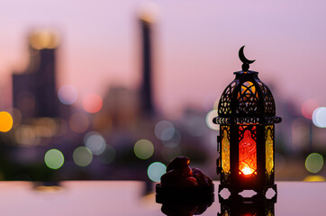 Lantern that have moon symbol on top and small plate of dates fruit with dawn sky and city bokeh light background for the Muslim feast of the holy month of Ramadan Kareem.