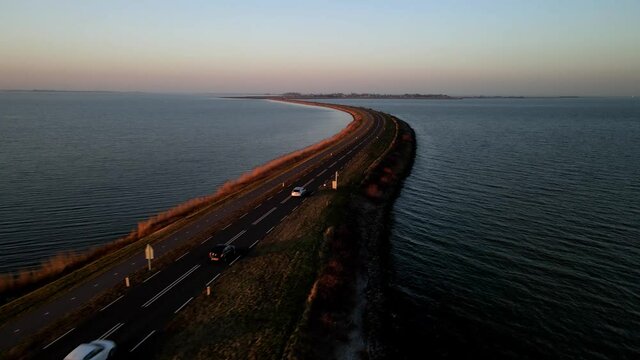 Three cars going over an empty road with water on two sides, The Netherlands near Marken.