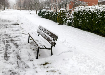 snowy bench on the side of the pedestrian road, snow covered the park area on a winter