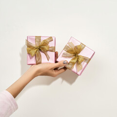 Presents for beloved women. Female hand holding two small wrapped gift boxes with golden bows against white background