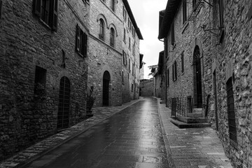 Assisi historic street with buildings built from stone after rain, black and white photo, Italy