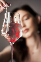 Drops of red blood paint in a glass of water, a woman looks at the glass.