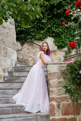 Fototapeta premium Beautiful woman with purple hair in a white wedding dress walks in the garden. Natural makeup