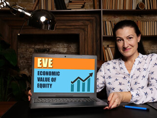 Woman showing laptop computer with  EVE ECONOMIC VALUE OF EQUITY icon on screen background, success...