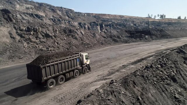 Aerial survey of truck. Dump truck carrying coal along in coal mine. Truck moving on dirt country road. Truck is driving along echnological road. Transportation of coal in trucks on road in open mine