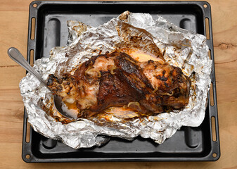 baked meat and fried onions on a baking sheet, pork ham on foil and wooden background, home cooking