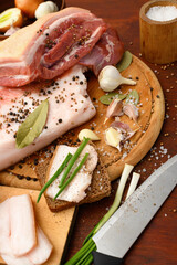 raw pork meat and lard with salt, spices and garlic on a cutting board, dark wooden background
