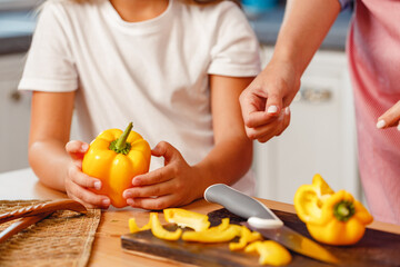 Hands of a woman and her kid cutting pepper on kitchen table
