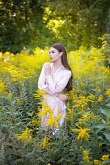 A beautiful woman in a light summer dress on a path and a forest meadow background.