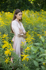 A beautiful woman in a light summer dress on a path and a forest meadow background.