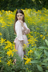Fototapeta premium A beautiful woman in a light summer dress on a path and a forest meadow background.