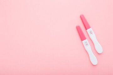 Pregnancy tests with one stripe and two stripes on light pink table background. Pastel color. Negative and positive result. Closeup. Empty place for text. Top down view.