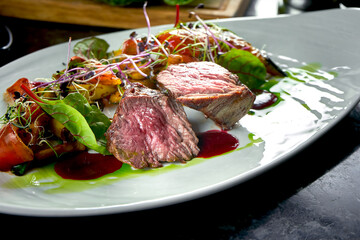 Medium rare beef medallions with vegetable garnish, served on a white plate. Dark marble background. Barbecue meat, restaurant food. Tasty steak
