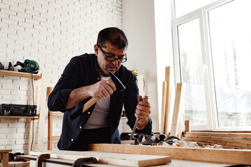 Middle-aged man carpenter working in a workshop with chisel and hammer