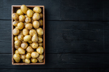 Baby potato raw heap, in wooden box, on black wooden table background, top view flat lay , with copyspace  and space for text