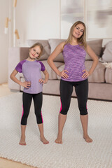 Mom and little daughter dressed in the same tracksuits  do exercises together at home