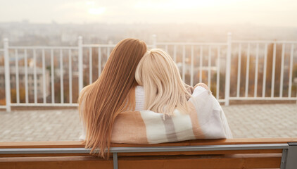Unrecognizable women hugging on bench on viewpoint