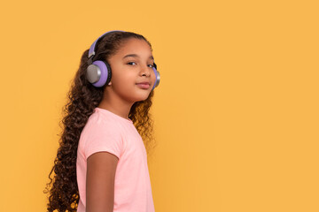 Young dark skinned  girl with long curly hair  in headphones enjoying music on a yellow background
