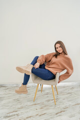 Fototapeta na wymiar Young attractive woman wearing sweatshirt and jeans on white background studio shot. Woman poses on chair.