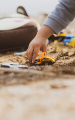 Manos de un chico joven jugando con vehículos de construcción en la arena