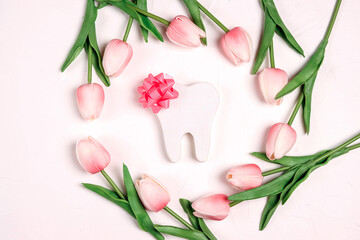 Obraz na płótnie Canvas Festive dental background with tooth and bow surrounded by pink tulips flowers on a white background with copy space for text.